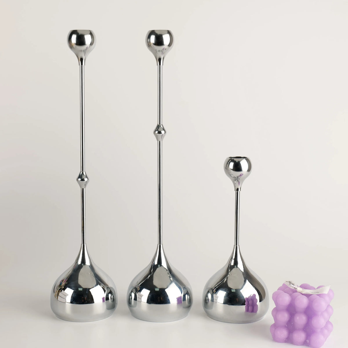 A set of three silver waterdrop design candle holders with elongated stems and rounded bases.