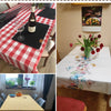 A collection of various fabric tablecloths and decor items, including a red and white checkered cloth, a white linen cloth wi