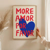 A framed canvas print featuring the text MORE AMOR FOR FAVOR in red and blue on a light background.