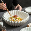 A white ruffled decorative bowl filled with yellow food topped with sauce and garnished with red threads, being served with c