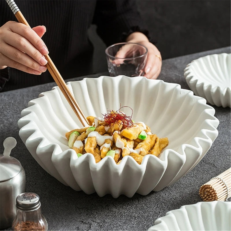 A white ruffled decorative bowl filled with yellow food topped with sauce and garnished with red threads, being served with c