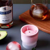 A pink stackable spherical ice mold sits next to a bottle of V.S.O.P. whiskey and a glass of amber liquid.