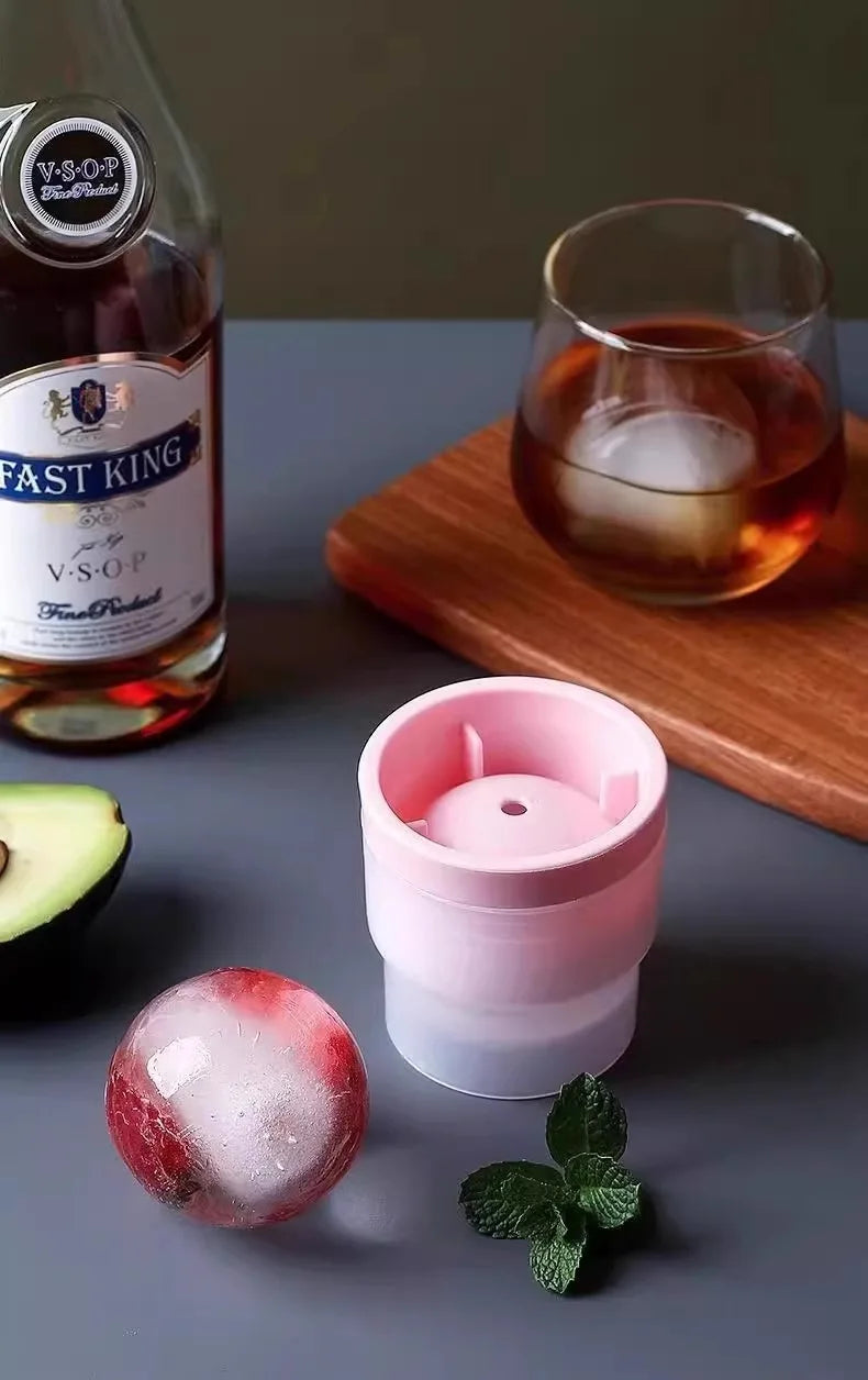 A pink stackable spherical ice mold sits next to a bottle of V.S.O.P. whiskey and a glass of amber liquid.