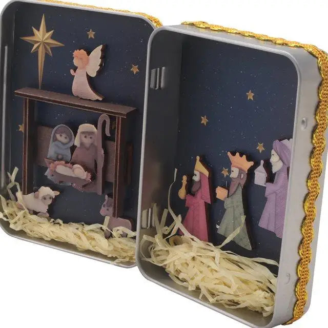 A tin box containing a hand-painted nativity scene decoration featuring figures and a star.