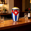 A colorful drum-style can holder with blue and white stripes and a red star is displayed on a wooden bar counter.