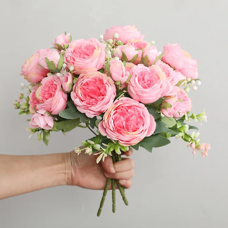 A hand holds a bouquet of pink silk peony roses for weddings and home decor.
