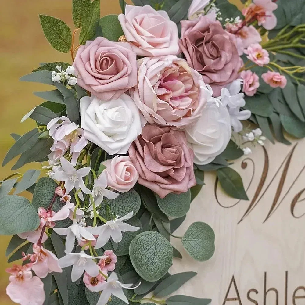 A floral arrangement featuring dusty rose and blush pink roses, white flowers, and green eucalyptus leaves for a wedding arch