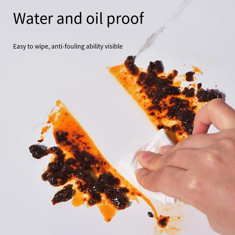 A hand wipes off oil and water from a dark, messy substance on a white surface.