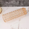 A long, cylindrical crystal gold flower vase with a textured pattern resting on a white marble surface.