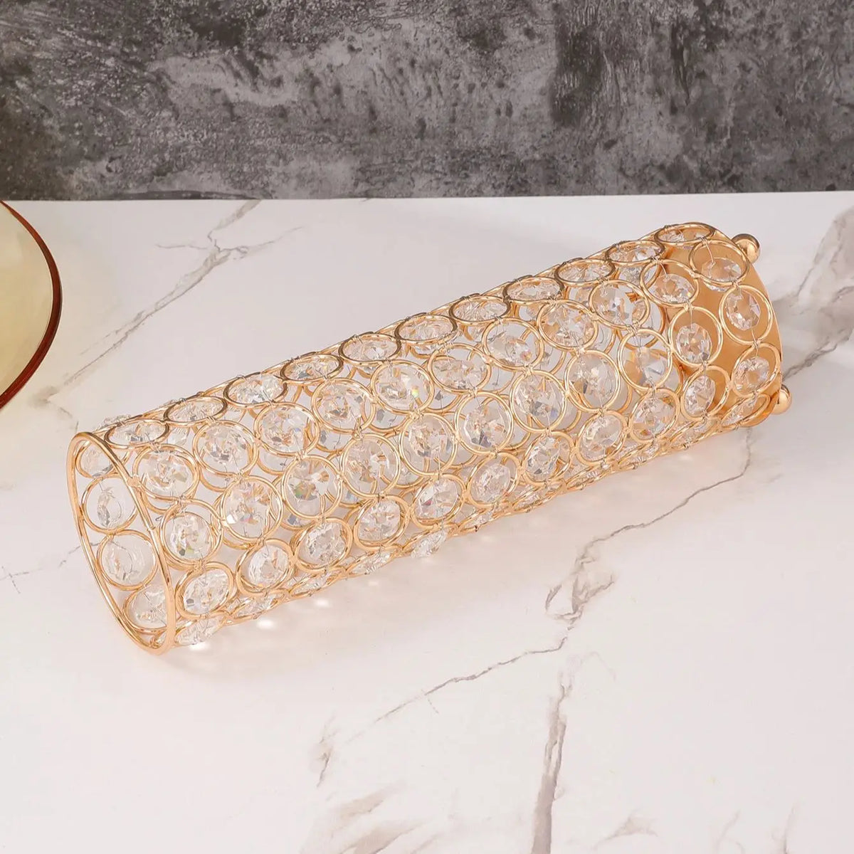 A long, cylindrical crystal gold flower vase with a textured pattern resting on a white marble surface.
