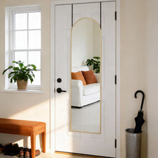 A full-length arched wall mirror with a gold aluminum frame hanging on a white door.