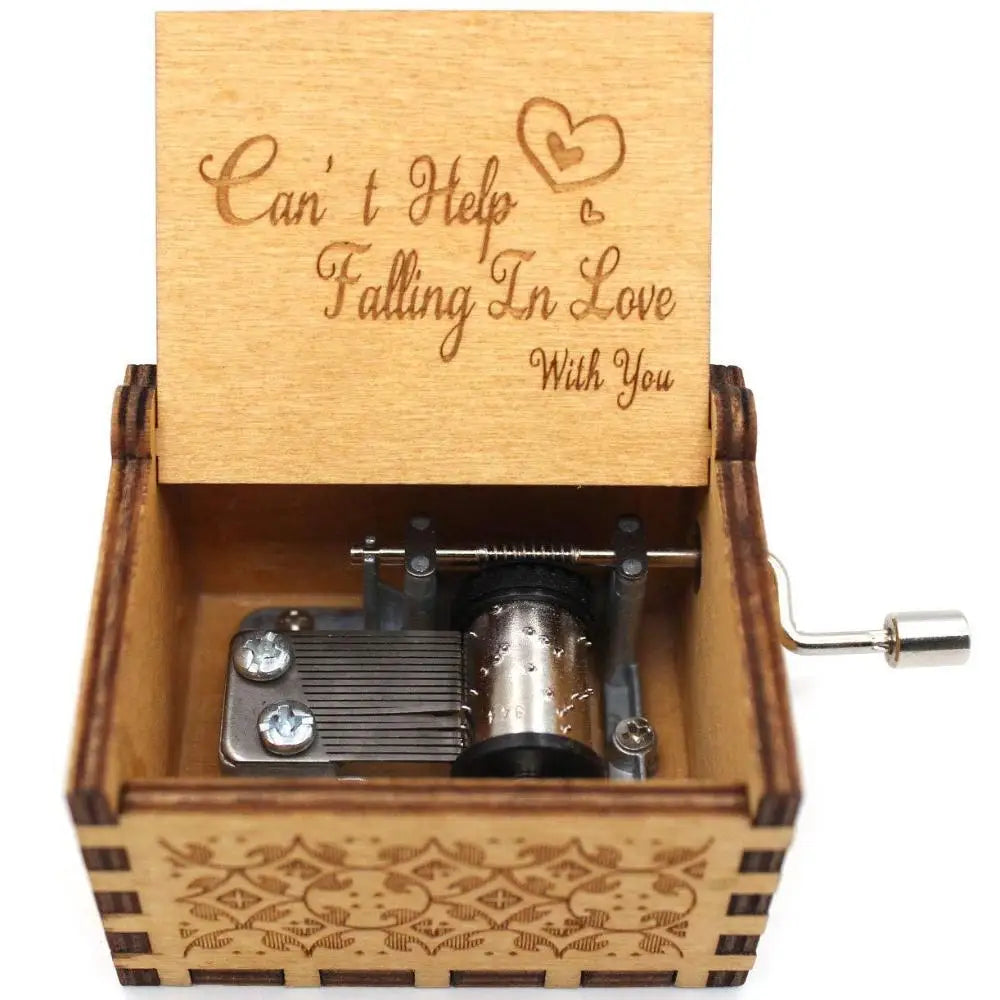 A vintage hand-cranked wooden music box with a lid engraved 'Can't Help Falling in Love' and a visible winding mechanism.