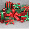 A collection of green and red gift boxes tied with satin ribbons and adorned with shiny red ornaments.