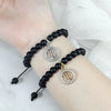 A black beaded bracelet with a silver zodiac sign charm worn on a wrist.