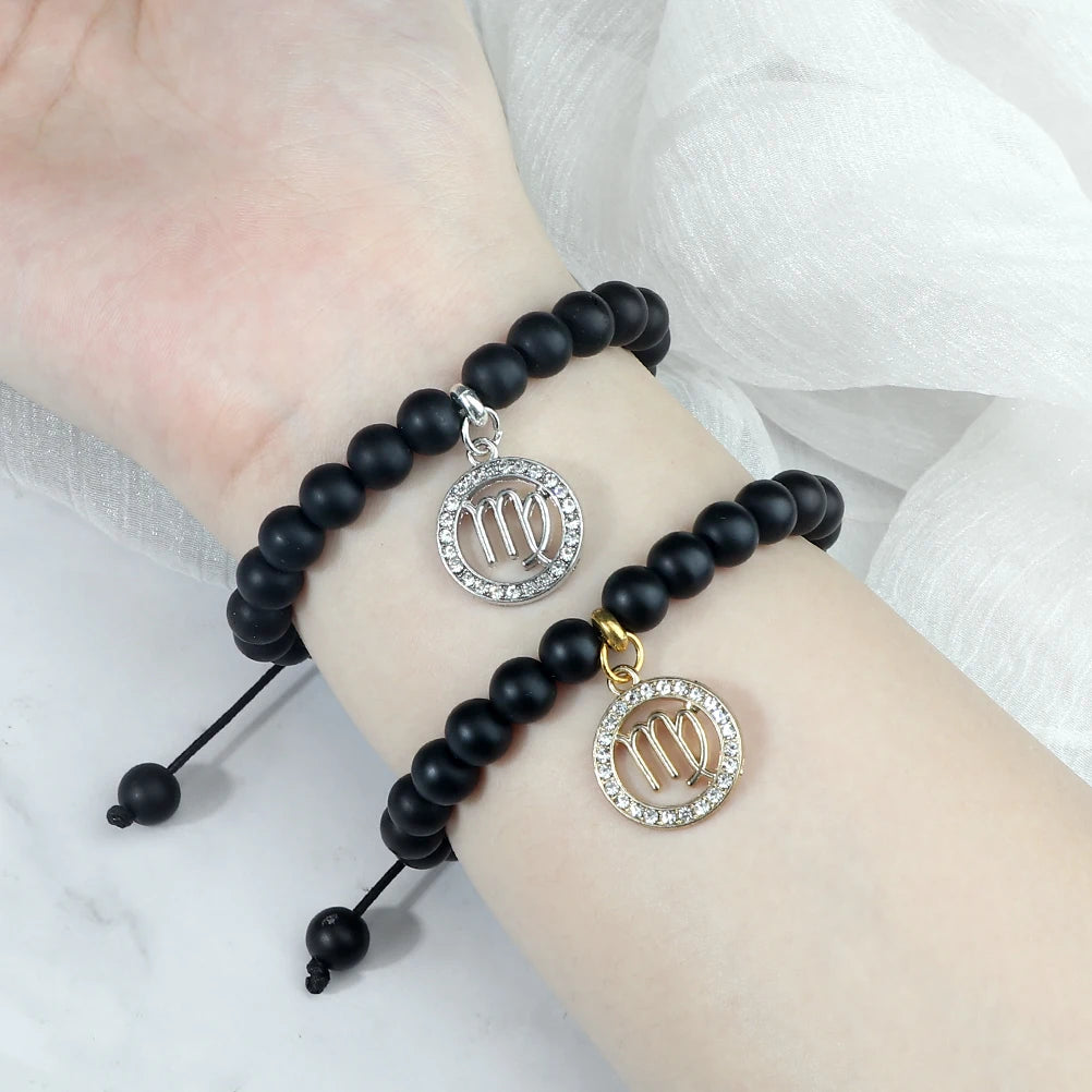 A black beaded bracelet with a silver zodiac sign charm worn on a wrist.