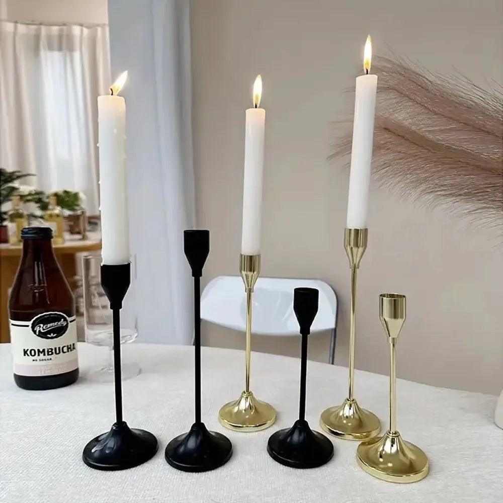 A set of three minimalist gold and black candle holders with white taper candles on a table.