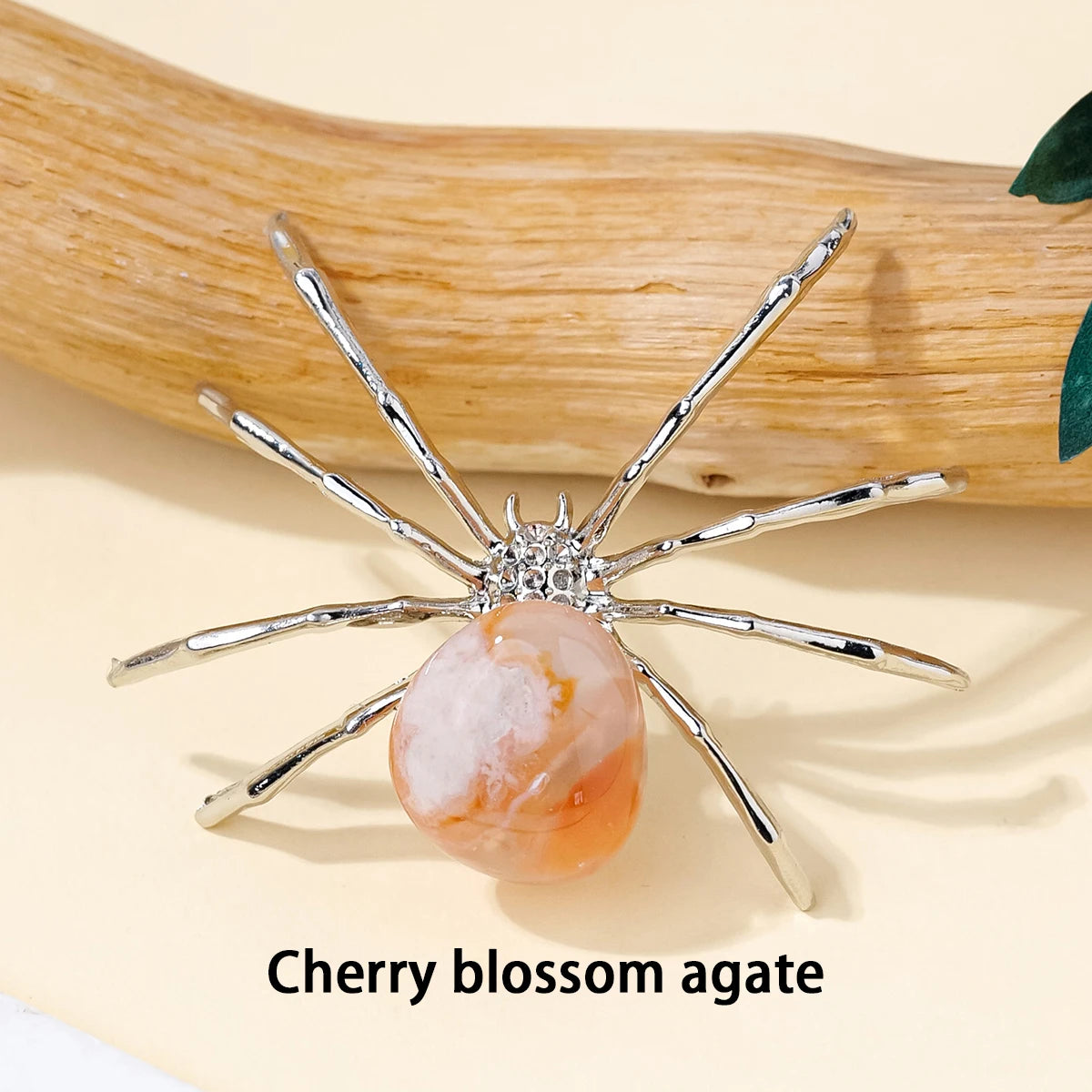 A handcrafted crystal spider figurine with silver legs and a cherry blossom agate body resting on a light background.