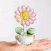 A handcrafted glass crystal sunflower figurine with a yellow bud and green stem resting on a hand.