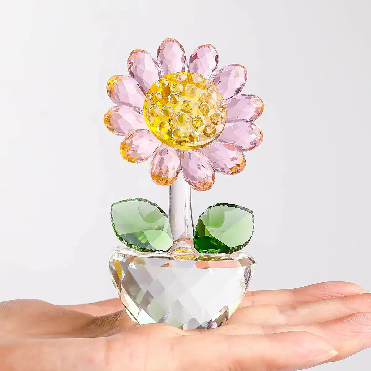 A handcrafted glass crystal sunflower figurine with a yellow bud and green stem resting on a hand.