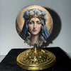 A round silver-framed ornament featuring a portrait of the Virgin Mary wearing a crown of blue flowers.