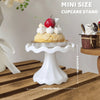 A white mini cupcake stand displaying a single cake topped with a red berry and whipped cream on a wooden surface.