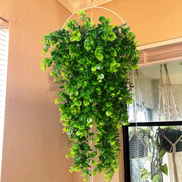 A lush green artificial eucalyptus plant hangs from a white hoop against a peach-colored wall.