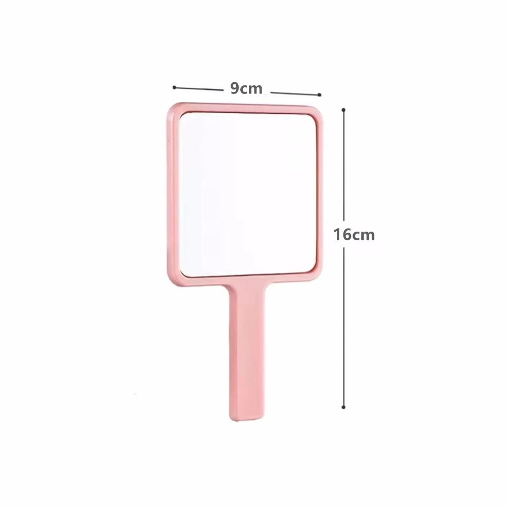 A pink compact handheld makeup mirror with a rectangular face and an ergonomic handle.