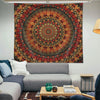 A large, circular tapestry featuring intricate mandala patterns in shades of red, orange, and brown hangs on a white wall abo