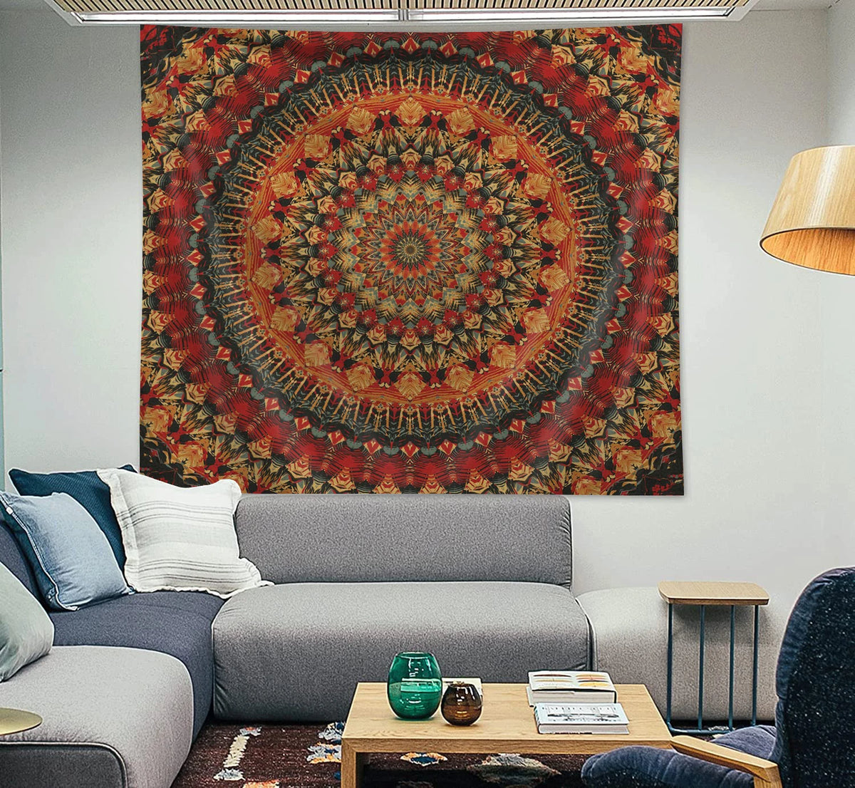 A large, circular tapestry featuring intricate mandala patterns in shades of red, orange, and brown hangs on a white wall abo