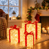 Three glowing red LED gift boxes wrapped in sheer gold paper sitting on a rug near a fireplace