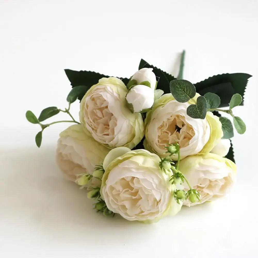 A bouquet of cream and white silk rose and peony artificial flowers with dark green leaves.
