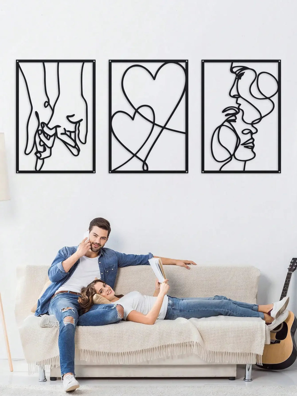 A couple relaxing on a couch in front of three framed black line art prints depicting holding hands, love, and kissing motifs