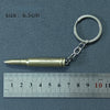A brass-colored alloy gun model keychain attached to a silver split ring, measured against a ruler.