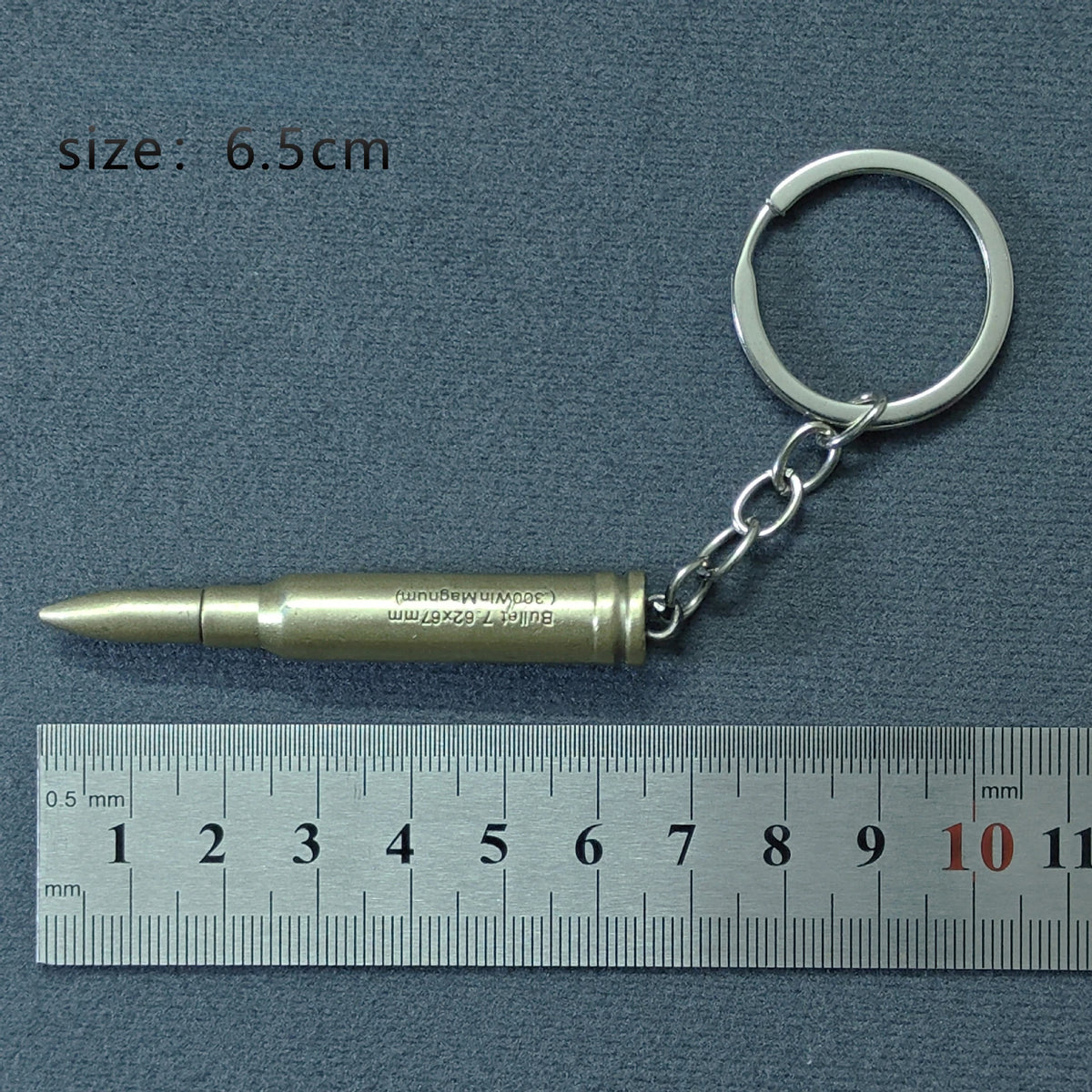 A brass-colored alloy gun model keychain attached to a silver split ring, measured against a ruler.