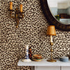 A decorative gold wall hook and a table display featuring a lamp and a small ceramic bowl against leopard print wallpaper.