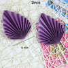 Two purple palm leaf cake toppers with pleated edges are displayed on a white macrame background.