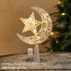 A clear glass crescent moon and star ornament with a warm white glow displayed on a stand.