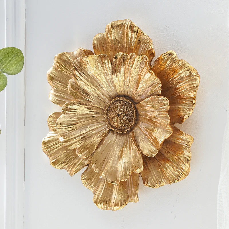 Gold resin wall art shaped like a large, layered flower blooming against a white background.