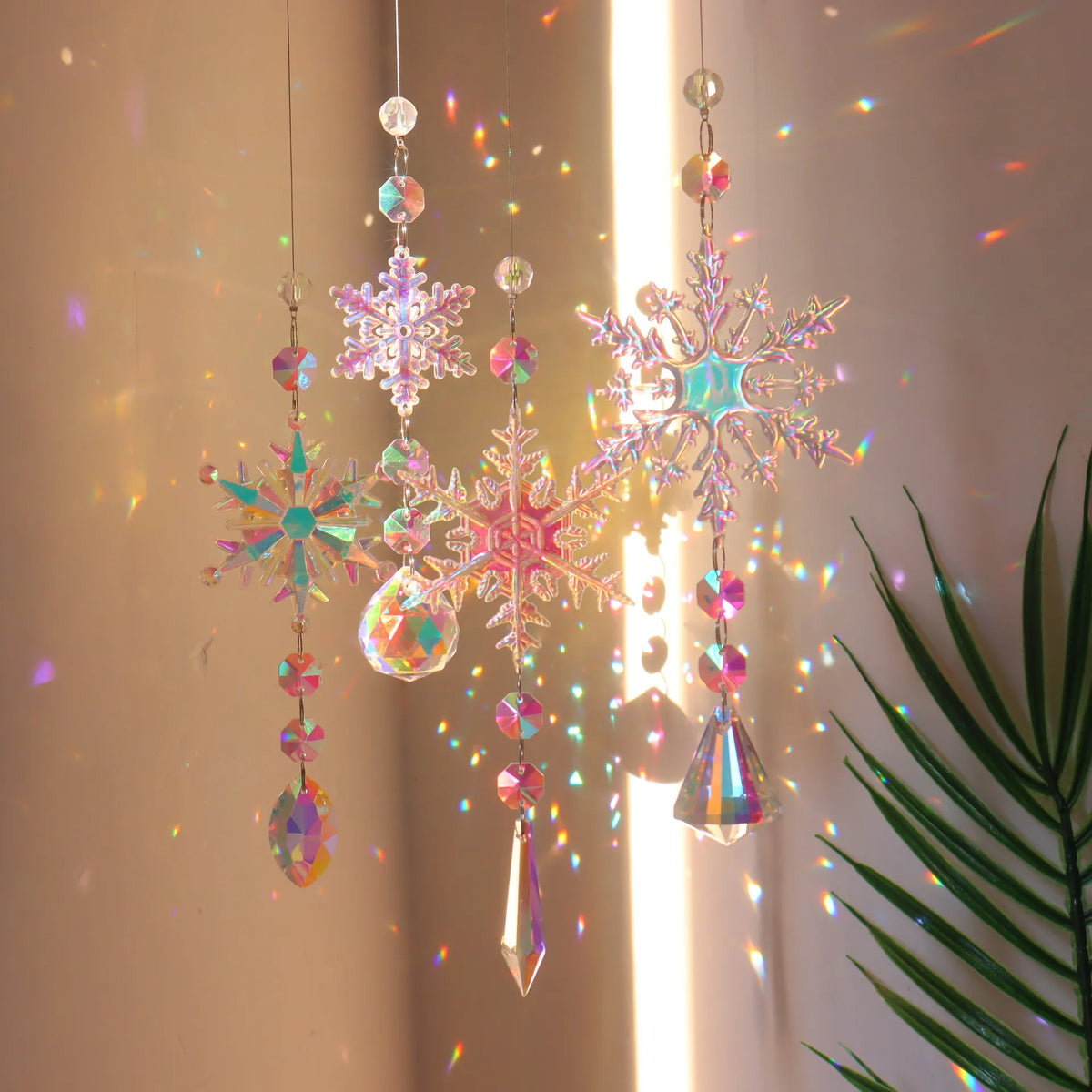 Crystal rainbow wind chime decor featuring sparkling pink and iridescent snowflakes hanging in a light beam.