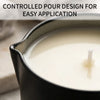A dark tin candle holder filled with white massage oil, showing a controlled pour design for easy application.