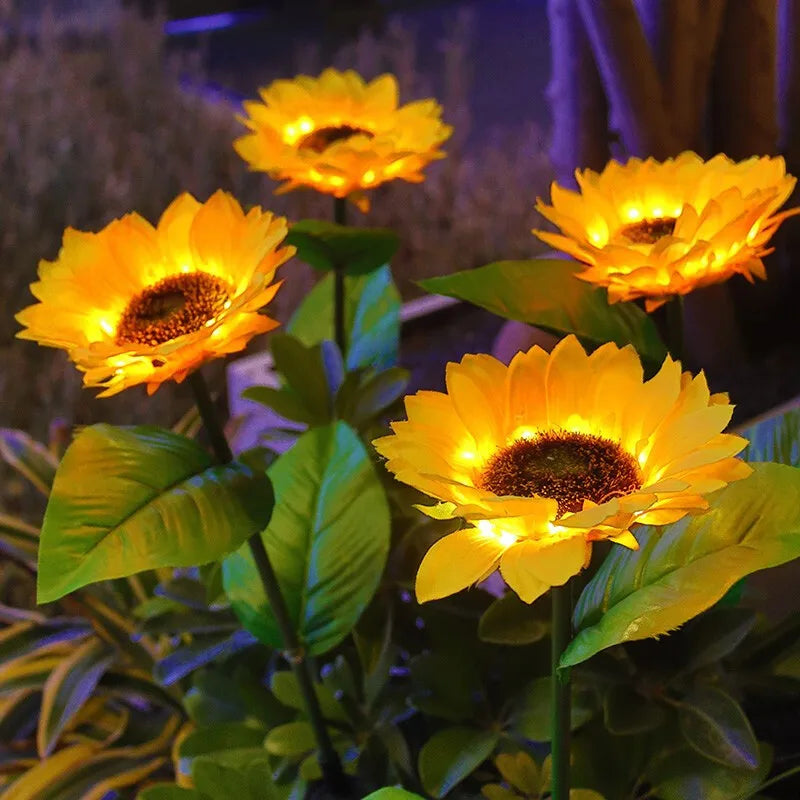A close-up of a bright yellow solar sunflower LED garden light blooming on green leaves.