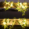 Golden string lights shaped like leaves illuminate a horizontal structure in an outdoor setting.