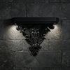 A black ornate Gothic wall shelf with intricate carvings mounted on a dark stone brick wall.