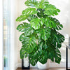 A large artificial monstera plant with vibrant green silk leaves displayed indoors next to a window.