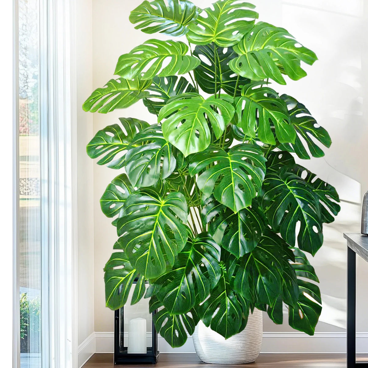 A large artificial monstera plant with vibrant green silk leaves displayed indoors next to a window.