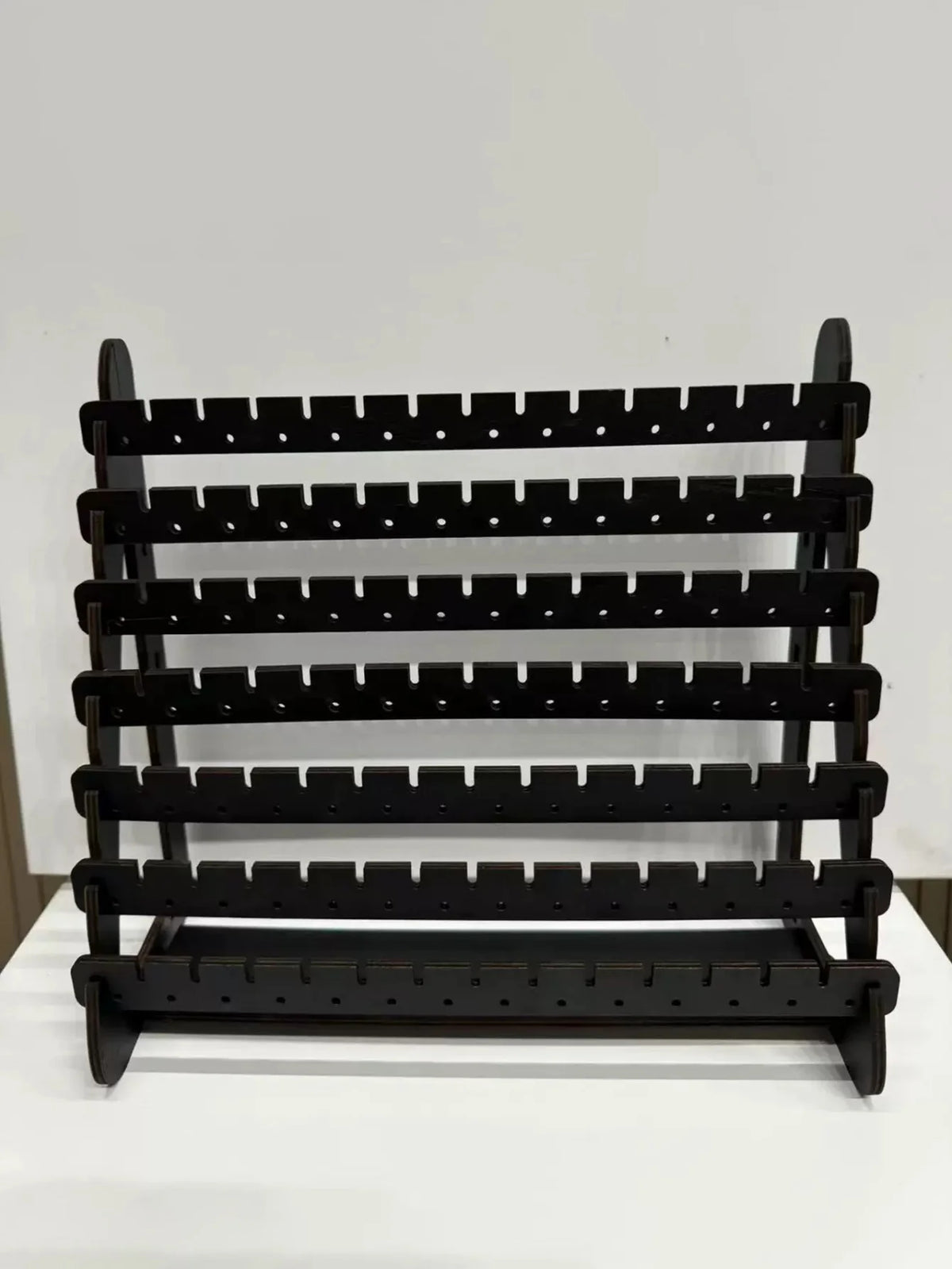 A black multilayer wooden earring organizer displaying jewelry.
