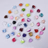 A collection of artificial silk rose petals in various shades of pink, red, purple, and green arranged on a white background.