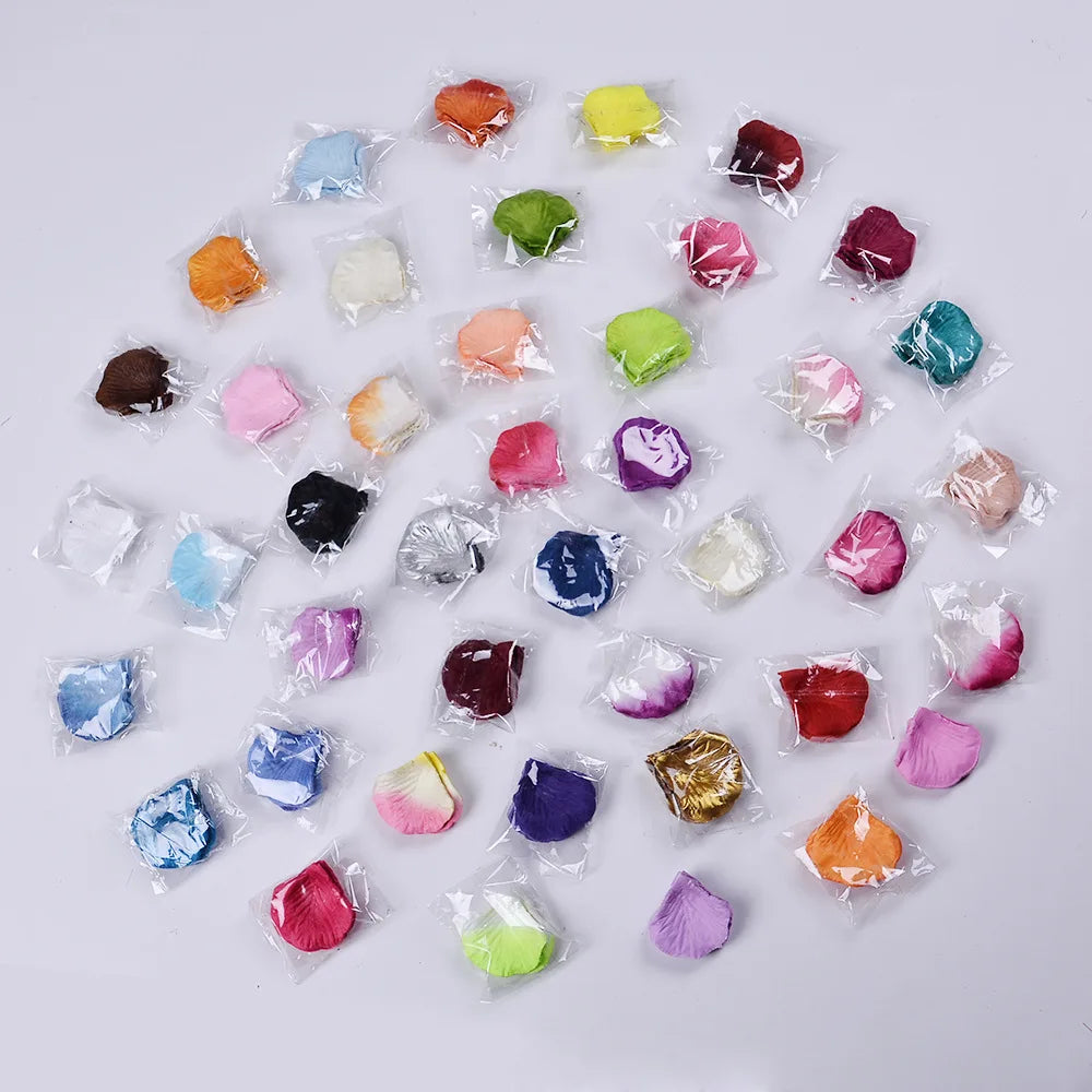 A collection of artificial silk rose petals in various shades of pink, red, purple, and green arranged on a white background.