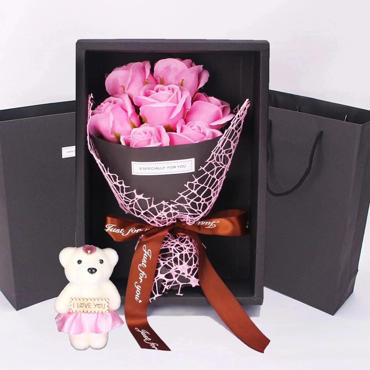 Un ramo de rosas rosadas atado con una cinta rosa transparente, exhibido dentro de una caja oscura con bolsas de regalo.