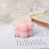 A set of two pink cube soy wax candles resting on a white notebook next to lace fabric.